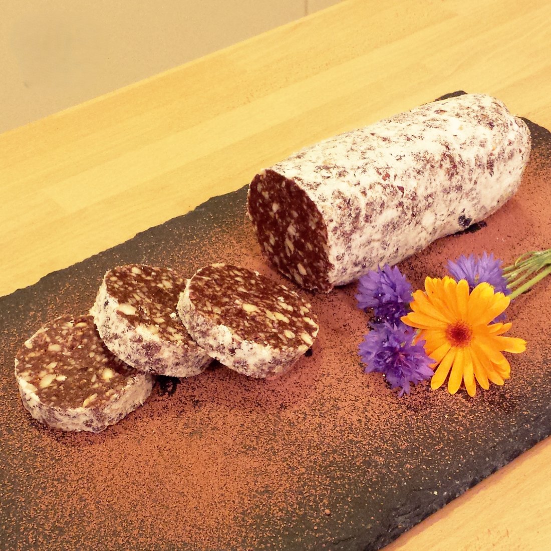 Salame di cioccolato a fette su tagliere di legno con un fiore
